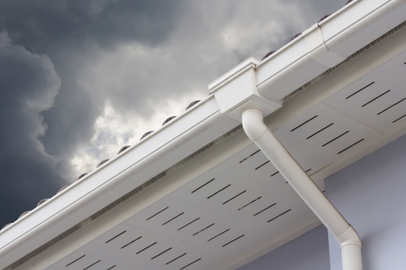 Upward shot of white gutter system and downspout beneath cloudy sky.